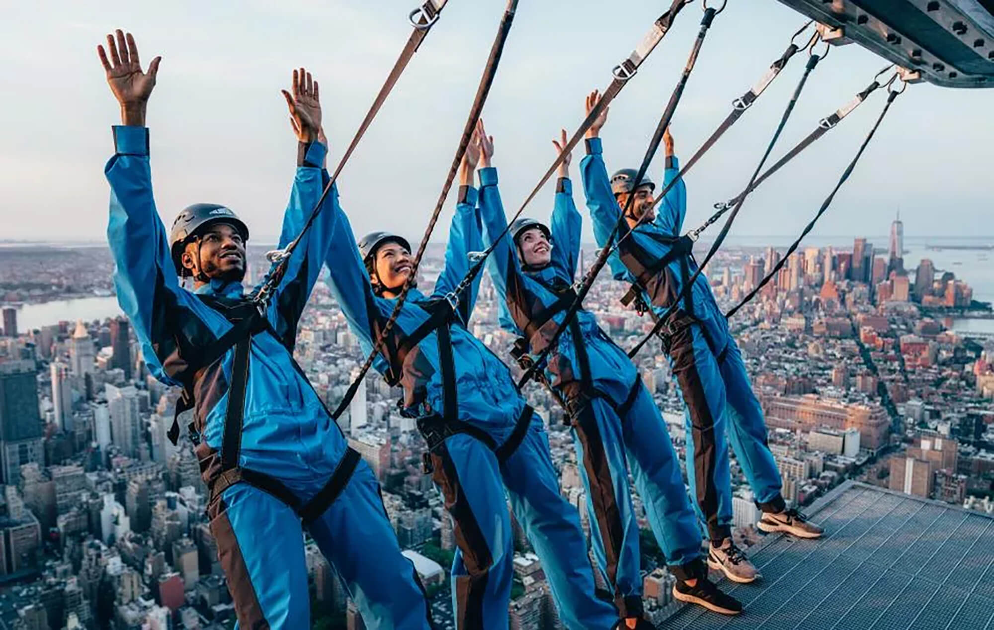 Four people raise their hands in the air in excitement as they lean back during City Climb at The Edge