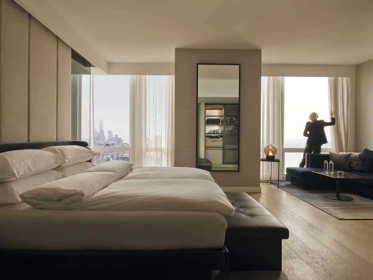 A king suite at Equinox, a woman pulling back curtains to let light in