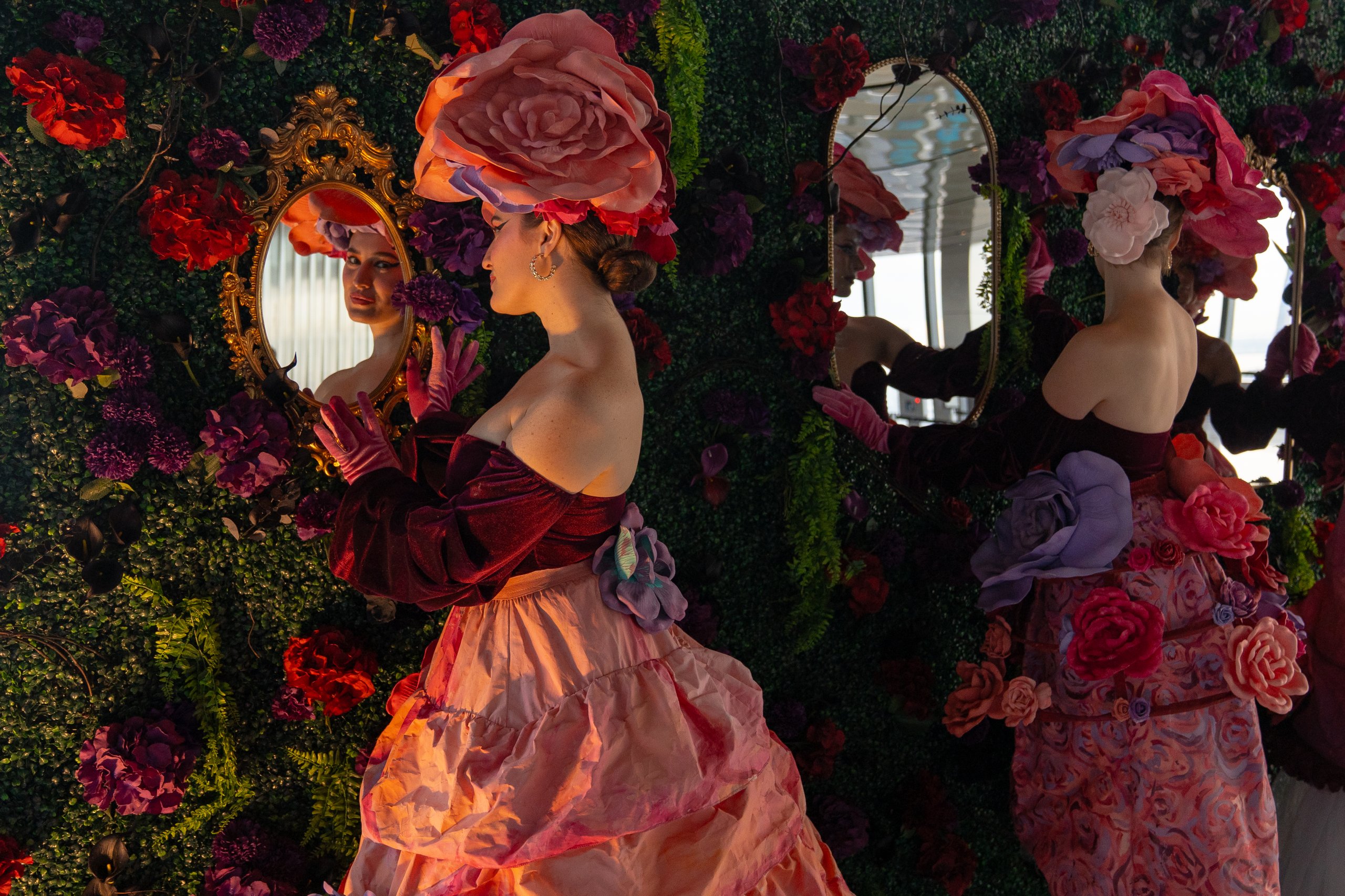 three women dressed in floral attire looking in mirrors for the garden of shadows